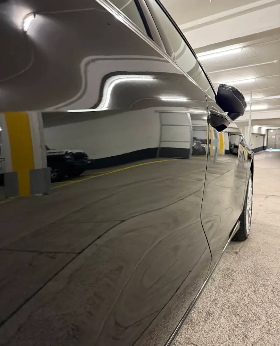 Spiegelnde Seitenpartie eines schwarzen Fahrzeugs nach der Politur, die Umgebung deutlich reflektiert